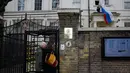 Dua orang menunggu untuk masuk saat seorang pria melepas bendera dari tiang di luar Kedutaan Besar Rusia di London, Rabu (14/3). Inggris diketahui mengusir 23 diplomat Rusia menyikapi kasus mantan agen ganda Rusia yang diduga diracun. (AP/Alastair Grant)