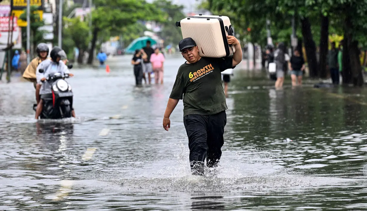 Ketinggian air akibat banjir mencapai sekitar 60 cm. Tampak dalam foto, seorang tamu hotel membawa kopernya sambil menerobos air di jalan yang tergenang banjir akibat hujan lebat di Legian Kuta, Denpasar, Bali, pada Selasa 24 Februari 2026. (SONNY TUMBELAKA/AFP)