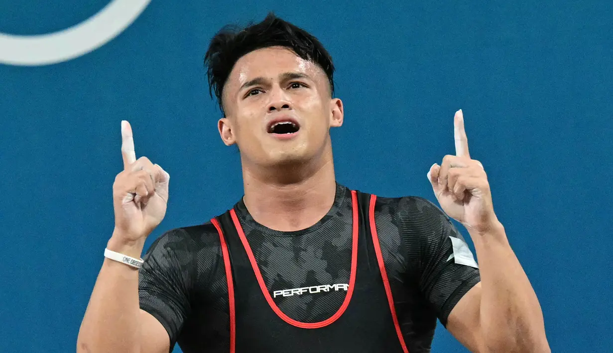 Rizki Juniansyah dari Indonesia melakukan selebrasi setelah memecahkan rekor di cabang olahraga angkat besi kelas 73kg putra selama Olimpiade Paris 2024 di South Paris Arena di Paris, pada 8 Agustus 2024 atau Jumat (9/8/2024) dini hari WIB. (Miguel MEDINA/AFP)