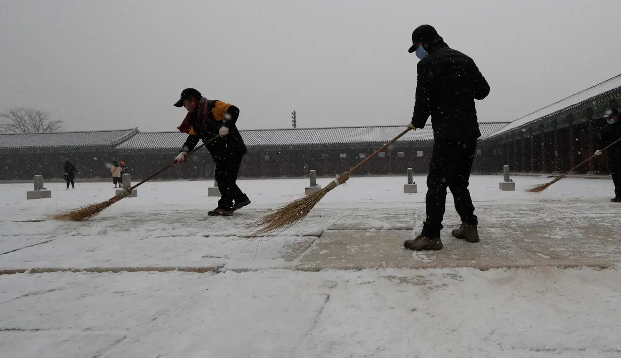 Para pria menyapu salju dengan sapu di Istana Gyeongbok di Seoul, Korea Selatan (13/12). Istana ini termasuk dari 5 istana besar dan merupakan yang terbesar yang dibangun oleh Dinasti Joseon. (AFP Photo/Lee Jin-man)