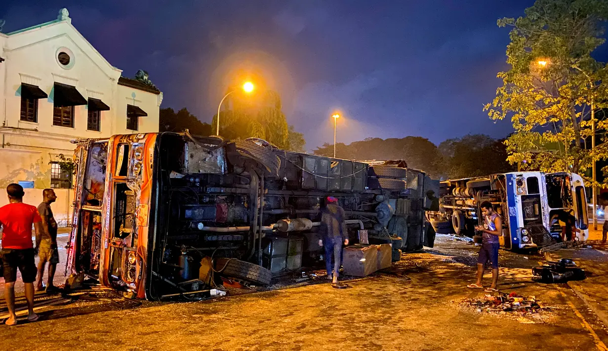 <p>Orang-orang melihat bus hancur yang tergeletak di dekat kediaman resmi Perdana Menteri Sri Lanka Mahinda Rajapaksa, di Kolombo pada 9 Mei 2022. Puluhan bus yang digunakan oleh loyalis Rajapaksa untuk melakukan perjalanan ke Kolombo pada hari sebelumnya dibakar atau rusak di seluruh negeri. (ISHARA S. KODIKARA / AFP)</p>
