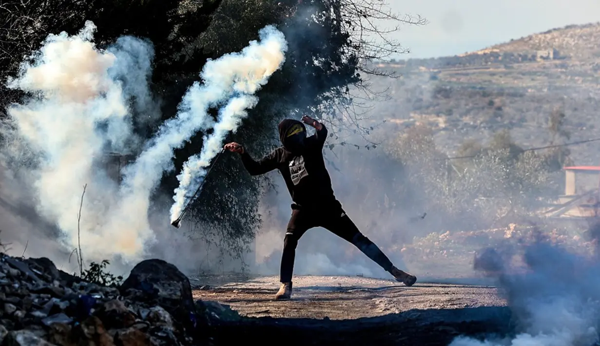 Seorang pemuda Palestina menggunakan ketapel untuk mengembalikan tabung gas air mata ke arah pasukan keamanan Israel saat bentrok pada demonstrasi menentang pengambilalihan tanah oleh Israel dekat pemukiman Yahudi Kedumim di Desa Kfar Qaddum, Tepi Barat, 21 Januari 2022. (JAAFAR ASHTIYEH/AFP)