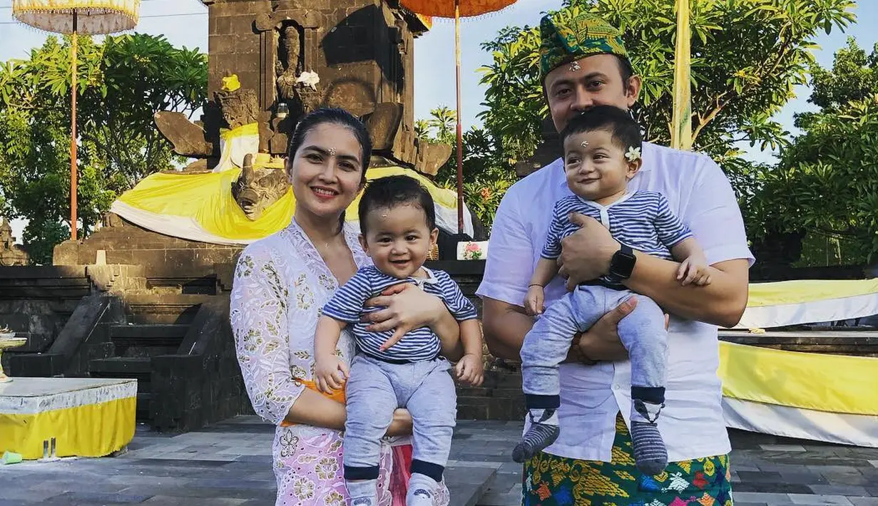 Terlihat diunggah di akun sang suami, Kadek Devi juga sempat terlihat beberapa kali dalam balutan kebaya Bali. Berpose di depan Pura, Kadek terlihat mengenakan kebaya brokat berwarna putih dengan selendang oranye, dan kain bernuansa merah muda sebagai bawahan. Foto: Instagram.