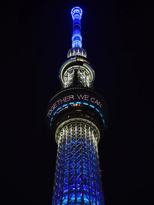 Menara Tokyo Skytree terlihat menyala dengan warna biru bertuliskan "Bersama Kita Semua Bisa Menang" di Tokyo, 5 April 2020. Ungkapan dukungan dan pesan harapan tersebut muncul di tengah merebaknya pandemi virus corona Covid-19. (CHARLY TRIBALLEAU/AFP)