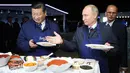 Presiden Rusia Vladimir Putin (kanan) mempersilakan Presiden China Xi Jinping (kiri) menyantap makanan saat membuat pancake bersama di sela Eastern Economic Forum di Vladivostok, Rusia, Selasa (11/9). (Sergei Bobylev/TASS News Agency Pool Photo via AP)