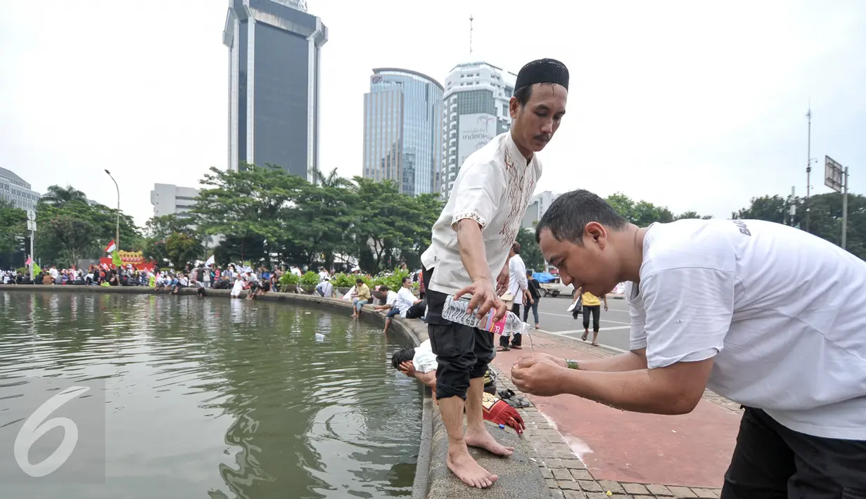 Demonstran menggunakan air mineral kemasan untuk wudhu sebelum menunaikan salat Jumat bersama di Bundaran Patung Kuda, Jakarta, Jumat (4/11). Sebagian massa demonstan gelar salat Jumat di area Bundaran Patung Kuda. (Liputan6.com/Yoppy Renato)