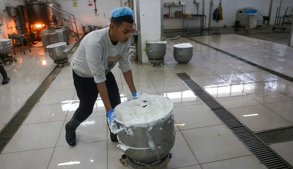 Saat ini, pabrik beroperasi dengan kapasitas yang masih disesuaikan. Tampak dalam foto, seorang karyawan Palestina memindahkan sebuah wadah berisi isian kue manis yang dikenal secara lokal sebagai "al-Shatwi" (kue musim dingin) Crimbo, saat pabrik Al-Arees secara bertahap melanjutkan produksinya setelah terhenti akibat perang, di Deir al-Balah, Jalur Gaza tengah pada 12 Januari 2026, (Bashar Taleb/AFP)