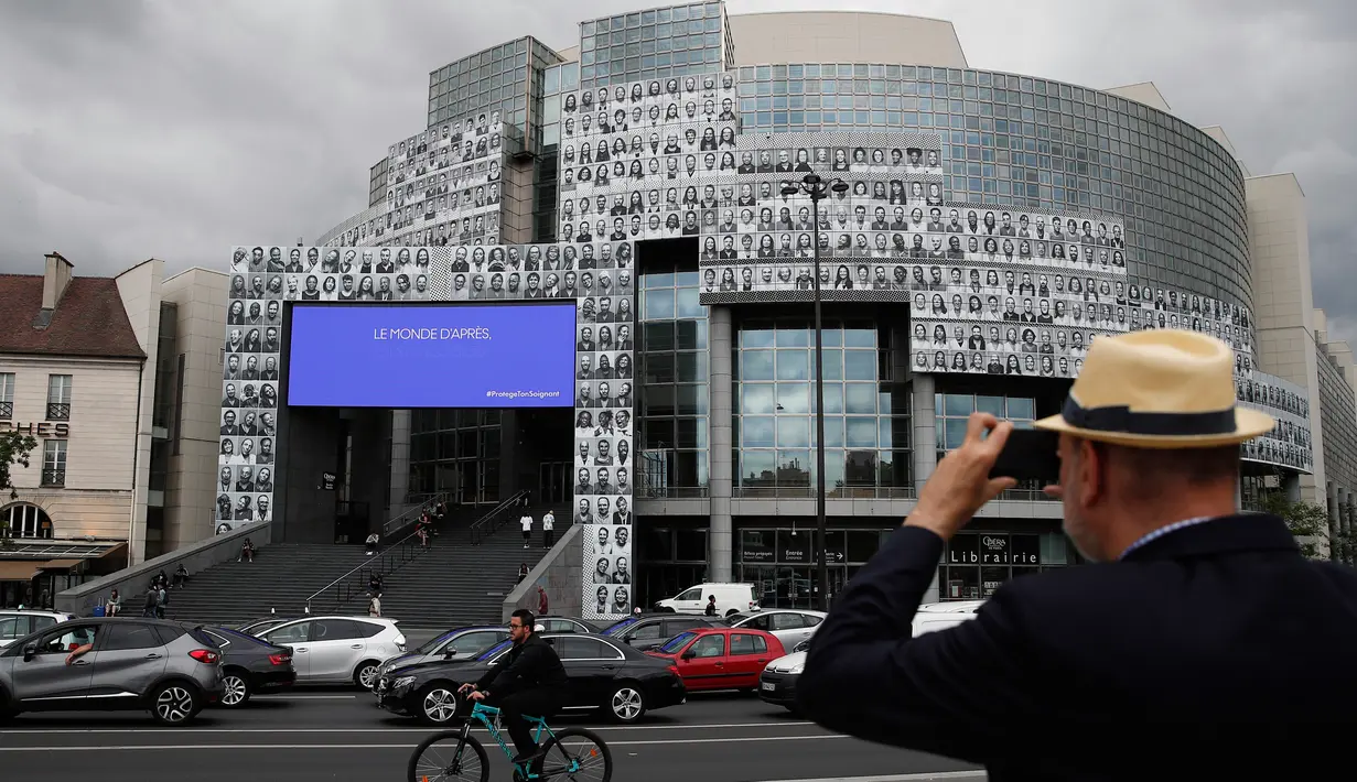 Seorang pria mengambil gambar potret para petugas kesehatan yang ditempelkan di bagian depan Bastille Opera di Paris, Prancis, Jumat (10/7/2020). Potret hitam putih itu untuk memberi penghormatan kepada pekerja medis yang berjuang menghadapi Corona Covid-19. (AP Photo/Francois Mori)