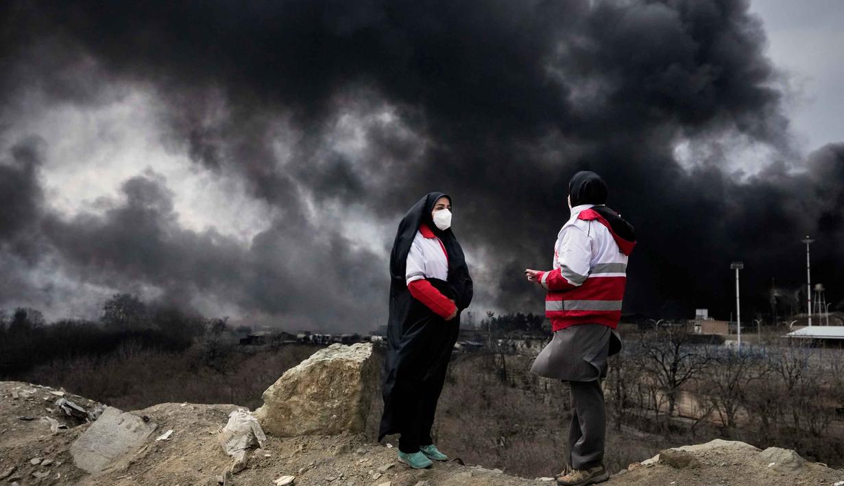 Beberapa laporan menyebut, adanya kebakaran besar di fasilitas kilang di ibu kota Iran, Teheran, setelah dihantam serangan udara pada Sabtu 7 Maret 2026 malam. Tampak dalam foto, dua wanita dari Palang Merah Iran berdiri saat kepulan asap tebal dari serangan AS-Israel terhadap fasilitas penyimpanan minyak Sabtu 7 Maret 2026 malam membubung ke langit di Teheran, Minggu, 8 Maret 2026. (AP Photo/Vahid Salemi)