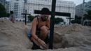 Seorang aktivis meletakkan salib di kuburan yang digali sebagai bentuk protes di pantai Copacabana, Rio de Janeiro, Kamis (11/6/2020). Kuburan-kuburan yang dihiasi bendera Brasil kecil itu untuk mengenang puluhan ribu pasien corona yang meninggal di negara tersebut. (AP Photo/Leo Correa)
