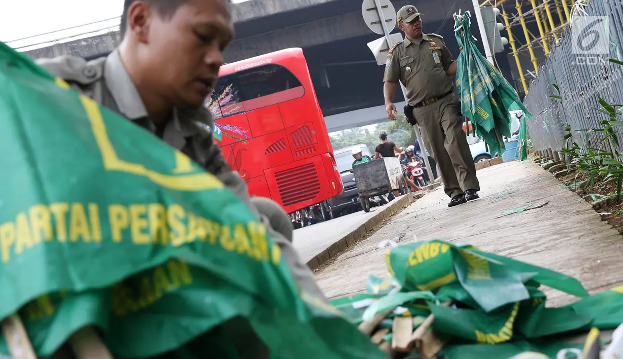 Petugas Satpol PP mencopot bendera partai politik di sepanjang pagar kawasan Pancoran, Jakarta. Selasa (18/7). Pencopotan dilakukan untuk menertibkan bendera partai politik liar yang memenuhi ruang publik di Ibukota. (Liputan6.com/Immanuel Antonius)