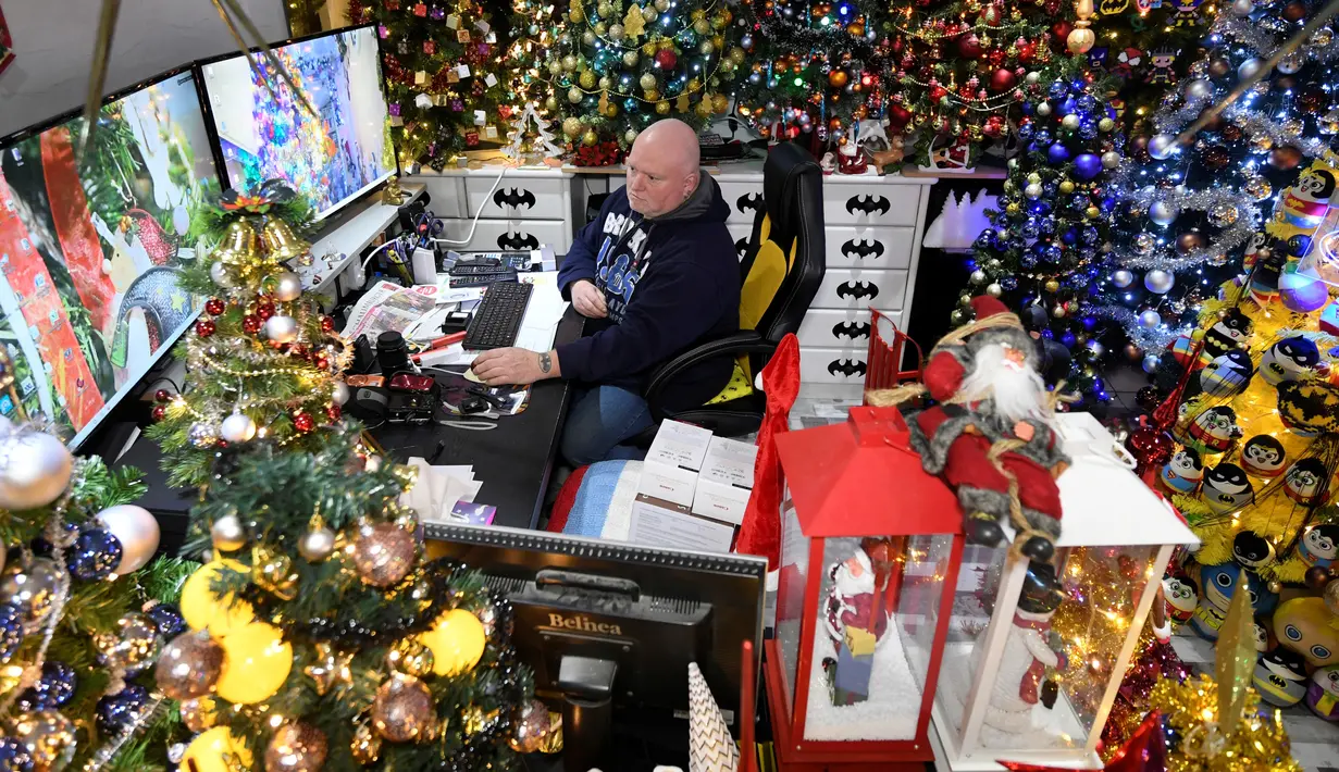 Thomas Jeromin duduk di depan layar komputer di antara pohon-pohon Natal yang dihias di rumahnya di Rinteln, Jerman, Minggu (8/12/2019). Thomas Jeromin memenuhi rumahnya dengan 350 pohon Natal di hampir tiap sudut rumah, mulai dari ruang tamu, dapur sampai kamar mandi. (Ina FASSBENDER/AFP)
