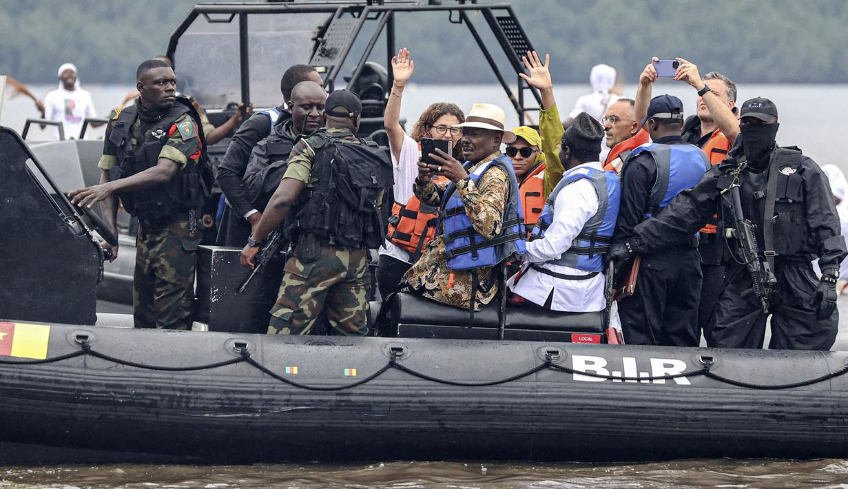 Pemain Paris Saint-Germain dan kapten Timnas Prancis, Kylian Mbappe melambaikan tangan saat tiba dengan kapal yang dikawal oleh Batalyon Intervensi Cepat, pasukan elit militer dan unit tempur Angkatan Bersenjata Kamerun, untuk mengunjungi desa ayahnya, Wilfrid Mbappe, di Djebale pada 8 Juli 2023. (AFP/Daniel Beloumou Olomo)