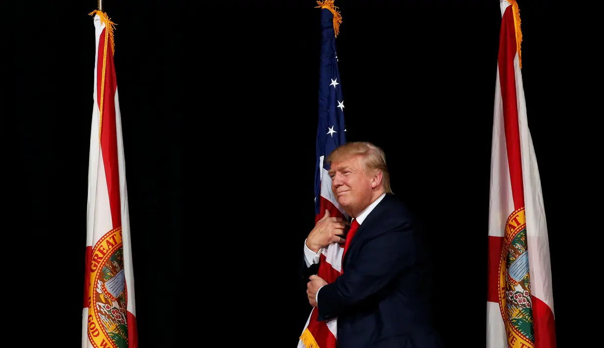 Capres AS dari Partai Republik, Donald Trump memeluk bendera AS saat melakukan kampanye menyapa pendukungnya di Tampa, Florida, AS (24/10). (REUTERS/Jonathan Ernst)