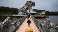 Foto pada 27 April 2019 memperlihatkan pengunjung berpose di depan bangunan berbentuk naga di Taman Air Ho Thuy Tien yang telah lama ditinggalkan di kota Hue, Vietnam. Taman air Ho Thuy Tien pertama kali dibuka untuk umum dalam keadaan setengah selesai pada tahun 2004. (Manan VATSYAYANA/AFP)