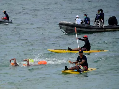 Para peserta bertanding sambil ditonton oleh kru pendukung dalam kompetisi renang Oceanman Bali 2021 di sebuah pantai di Sanur, Denpasar, Bali, Sabtu (18/9/2021). Oceanman Bali 2021 akhirnya sukses digelar setelah beberapa kali ditunda. (SONY TUMBELAKA/AFP)