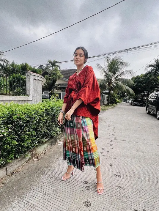 Eva Celia juga memiliki gaya khas yang simpel, namun edgy. Di sini ia menampilkan gaya mengenakan wastra. Baju bodo merah dipadunya mengenakan sarung sebagai rok bernuansa kuning kehijauan yang serasi. [Foto: Instagram/evacelia]