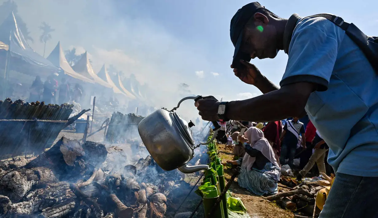 Seorang peserta mengisi tabung bambu dengan santan saat memasak lemang, hidangan nasi ketan tradisional yang dimasukkan ke dalam tabung bambu dan diisi dengan santan yang kemudian diletakkan di atas api, selama acara memasak massal di Blang Pidie, Kabupaten Aceh Barat Daya, Aceh, pada Sabtu 25 April 2026. (CHAIDEER MAHYUDDIN/AFP)