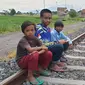 Tiga anak-anak terlihat duduk di atas bantaran rel kereta api Stasiun Garut, Jawa Barat ngabuburit sambil menunggu waktu iftor tiba. (Liputan6.com/Jayadi Supriadin)