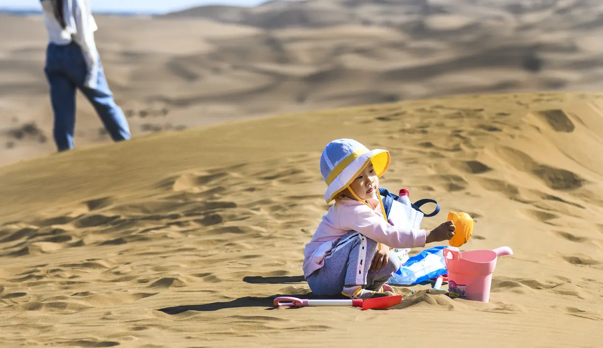 Seorang anak bermain pasir di kawasan wisata Gurun Kum Tag di Wilayah Shanshan, Kota Turpan, Daerah Otonom Uighur Xinjiang, China barat laut (22/9/2020). Gurun tersebut saat ini mencatat peningkatan arus wisatawan. (Xinhua/Wang Fei)