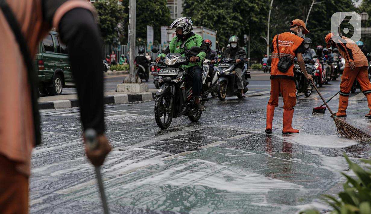 Sejumlah pengendara motor berkendara dengan hati-hati saat anggota Penanganan Prasarana dan Sarana Umum (PPSU) membersihkan tumpahan oli di kawasan Jalan Thamrin, Jakarta, Selasa (4/10/2022). Pembersihan ceceran tumpahan oli tersebut agar pengendara motor tidak terjatuh. (Liputan6.com/Faizal Fanani)