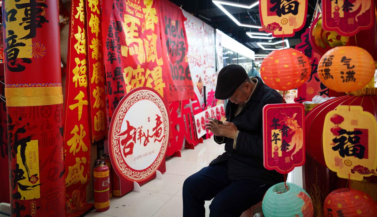 Perayaan ini menjadi mudik massal kembali ke kampung halaman untuk bertemu keluarga. Imlek juga menjadi simbol peralihan musim dari dingin ke semi. Tampak dalam foto, seorang pria duduk di dalam sebuah kios yang dikelilingi dekorasi Tahun Baru Imlek di sebuah pasar di Beijing, China, Rabu 4 Februari 2026. (AP Photo/Vincent Thian)
