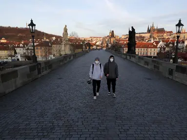 Dua pria muda yang mengenakan masker berjalan melintasi Jembatan Charles yang sepi di Praha, Republik Ceko, Senin (16/3/2020). Pemerintah Ceko memberlakukan pembatasan terhadap seluruh warganya dalam upaya mengendalikan penyebaran virus corona COVID-19. (AP Photo/Petr David Josek)