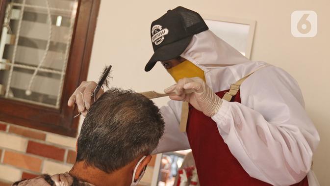 Tukang cukur mengenakan APD saat memotong rambut di halaman rumah pelanggan, Kelapa Dua, Depok, Jawa Barat, Senin (27/4/2020). Penerapan PSBB Kota Depok membuat tukang cukur tersebut menerima jasa panggilan ke rumah dan mengenakan APD untuk mencegah penularan COVID-19. (Liputan6.com/Herman Zakharia)