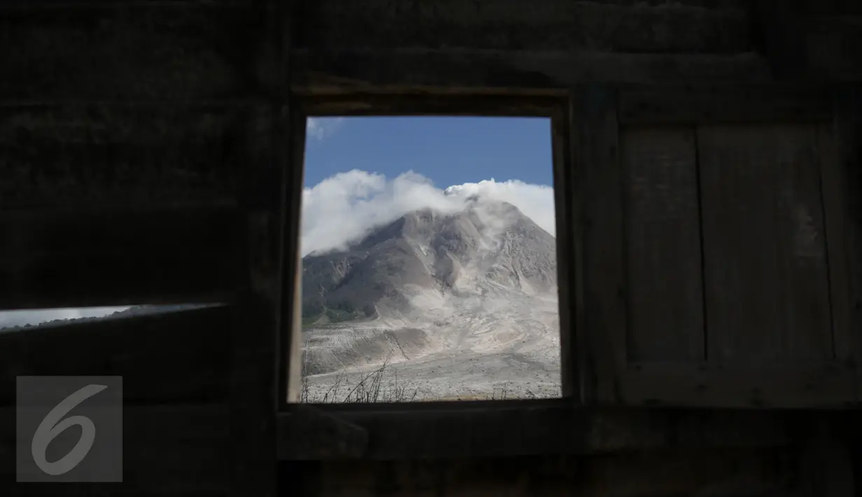 Gunung Sinabung terlihat dari puing jendela rumah yang rusak akibat luncuran awan panas pada April 2015 di Desa Sibintun, Karo, Sumatera Utara, Minggu (5/7). Akibat letusan Sinabung, desa tersebut sudah tak lagi berbentuk. (Liputan6.com/Johan Tallo)
