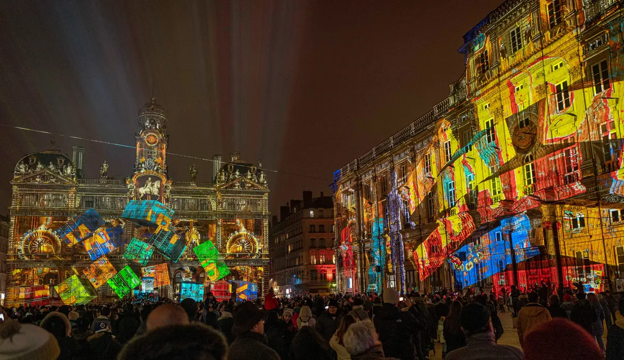Orang-orang melihat balai kota Lyon (tengah) dan alun-alun Place des Terreaux yang diterangi cahaya lampu selama Festival of Lights (Fete des Lumieres) di kota Lyon, Prancis, Kamis (5/12/2019). Festival Cahaya ini merupakan salah satu kegiatan yang paling terkenal di Lyon. (ROMAIN LAFABREGUE / AFP)