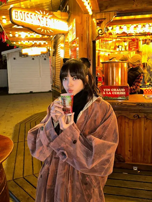 <p>Lisa mengenakan pakaian berlapis dengan bagian luar jaket oversize. Personel Blackpink tersebut juga memegang gelas berisi minuman untuk menghangatkan badannya. (Instagram/@lalalalisa_m)</p>