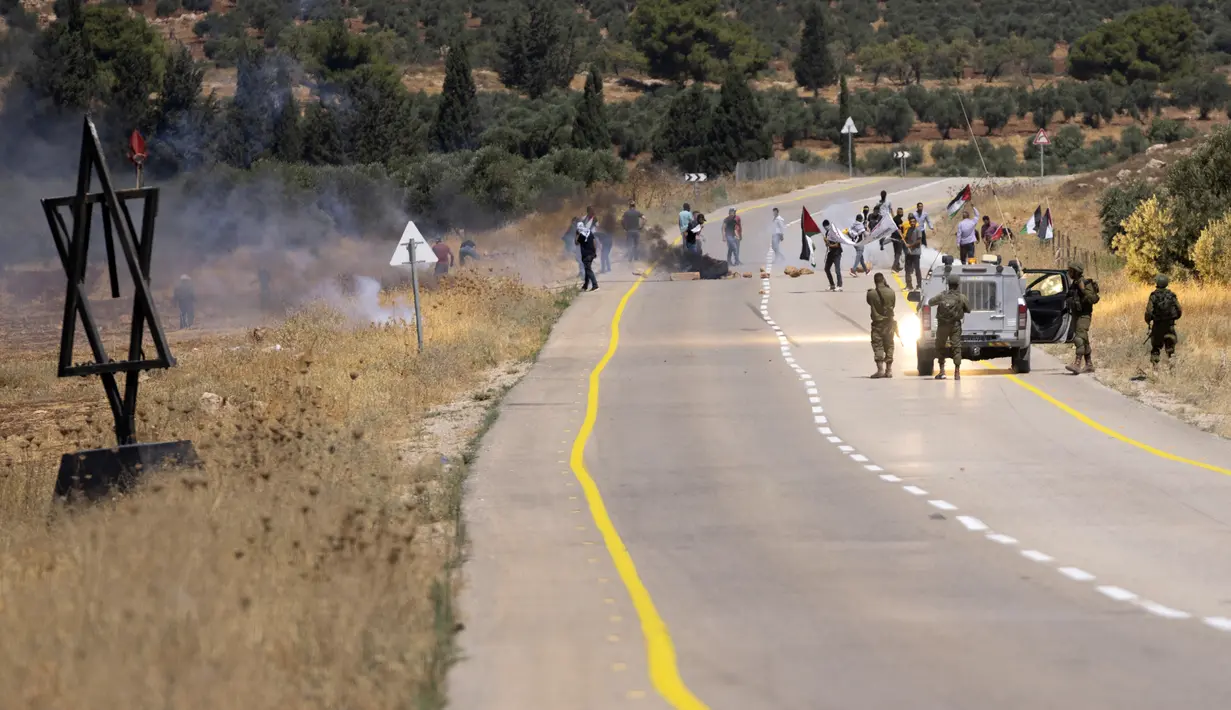 Tentara Israel menembakkan gas air mata untuk membubarkan pengunjuk rasa Palestina saat membakar ban dan memblokir jalan yang melewati Desa Mughayer, Tepi Barat, utara Ramallah, 29 Juli 2022. Warga Palestina yang memprotes aktivitas permukiman Israel memblokir jalan utama dan bentrok dengan pemukim Israel, sementara tentara menembakkan gas air mata untuk membubarkan mereka. (AP Photo/Nasser Nasser)