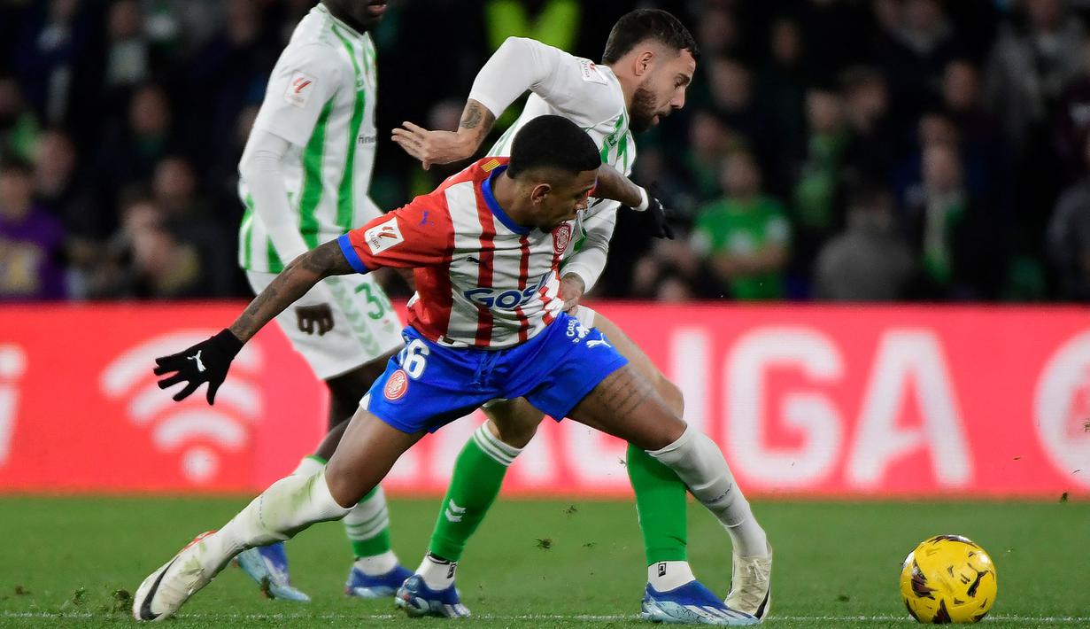 Pemain Girona, Savio Moreira (tengah) berebut bola dengan pemain Real Betis, Aitor Ruibal pada laga pekan ke-18 Liga Spanyol 2023/2024 di Benito Villamarin Stadium, Sevilla, Spanyol, Jumat (22/12/2023) dini hari WIB. (AFP/Cristina Quicler)