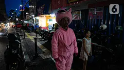 Warkuatno (41) bersama anak sulungnya, Bunga (9) berjalan kaki di pinggir Jalan Raya Fatmawati, Jakarta, Rabu (6/1/2021). Mantan sopir Metromini 75 ini menjadi badut keliling sejak bulan Maret lalu, tak lama setelah kasus corona COVID-19 terdeteksi di Indonesia. (Liputan6.com/Faizal Fanani)
