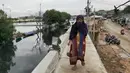 Warga melintas di atas tanggul pantai di Kamal Muara, Jakarta, Rabu (26/12). Pembangunan tanggul pantai di Kamal Muara dengan panjang 740 meter yang akan rampung pada 2020. (Liputan6.com/Herman Zakharia)