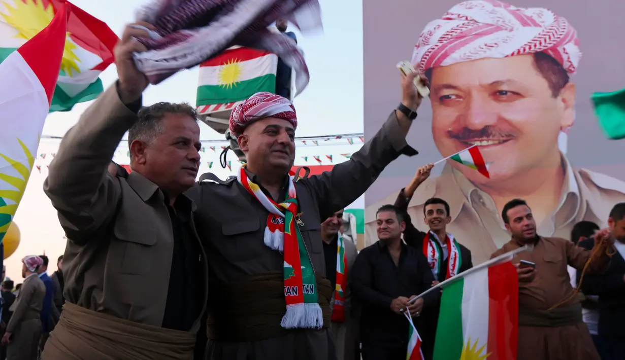 Warga Kurdi Irak berkumpul sambil melambai-lambaikan bendera Kurdi di samping poster Pemimpin Kurdi, Massoud Barzani saat melakukan aksi untuk meminta referendum kemerdekaan di Arbil, Irak utara (13/9). (AFP Photo/SAfim Hamed)