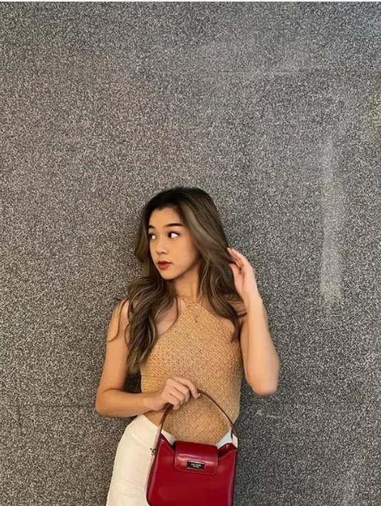 Gabriella Eka Putri juga tampak menenteng tas Kate Spade. Ia membawa Holiday Sam Icon Mini Bag berwarna merah gelap, meniru warna batu bata permata rubi dalam balutan halter tank berwarna nude dan rok putih. Foto: Document/Kate Spade New York.