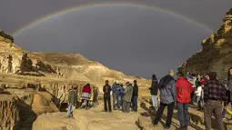 Pelangi terlihat saat warga Israel melihat banjir bandang yang terjadi menyusul hujan lebat di gurun Negev di sebelah timur kota Dimona Israel pada 26 Desember 2022. Hujan deras mengguyur Israel utara, dataran pantai, Yerusalem, dan sebagian Negev utara, termasuk kilat dan angin kencang di beberapa daerah. (AFP/Menahem Kahana)