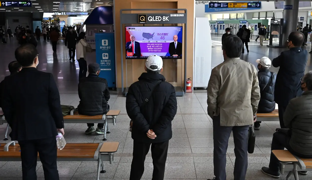 Orang-orang menonton program berita televisi tentang pemilihan presiden (pilpres) AS yang menampilkan gambar Presiden Donald Trump (kiri) dan calon presiden dari Partai Demokrat Joe Biden (kanan), di sebuah stasiun kereta api di Seoul, Korea Selatan pada Rabu (4/11/2020). (Photo by Jung Yeon-je/AFP)