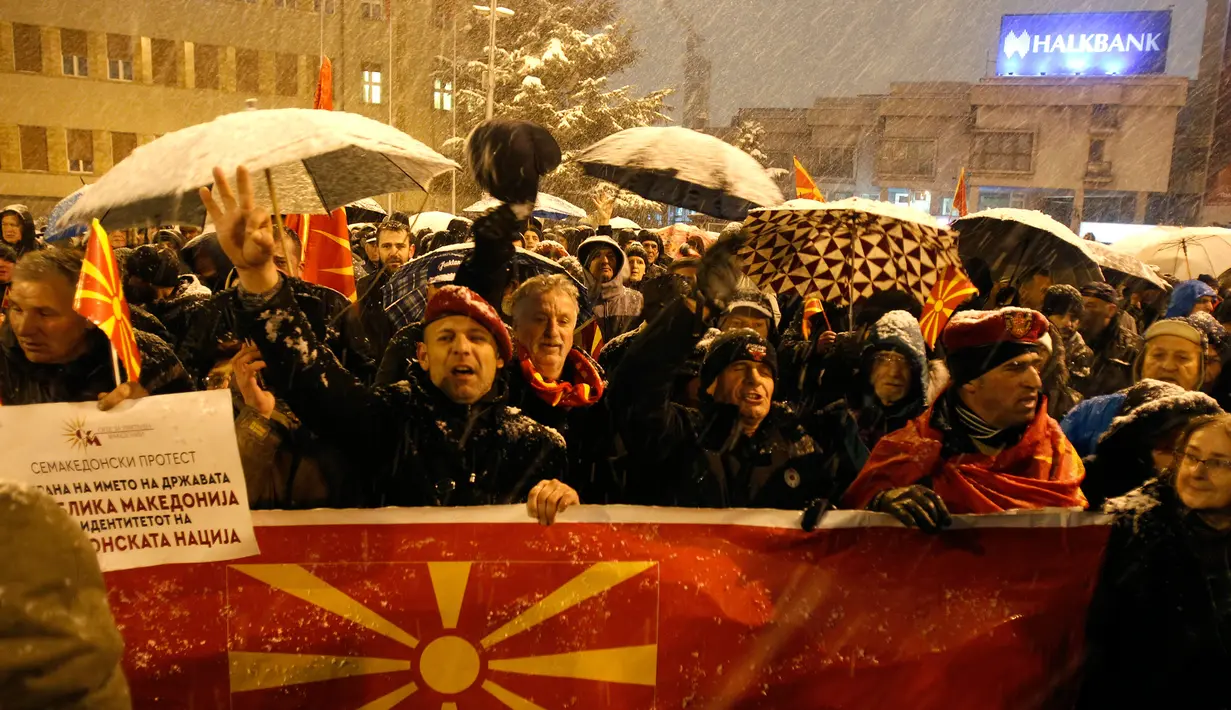 Warga membentangkan bendera Macedonia saat menggelar protes di depan gedung Parlemen, Skopje, Selasa (27/2). Di tengah hujan salju dan temperatur ekstrem, mereka turun ke jalan memprotes wacana pengubahan nama negara mereka. (AP/Boris Grdanoski)