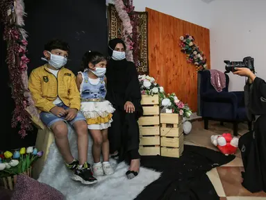 Seorang wanita dan anak-anak mengenakan masker berpose saat difoto  pada liburan Idul Fitri Muslim selama pandemi virus coronavirus COVID-19 di studio foto Palestina Faten Issa's studio di Rafah di Jalur Gaza selatan (27/5/2020). (AFP/Said Khatib)