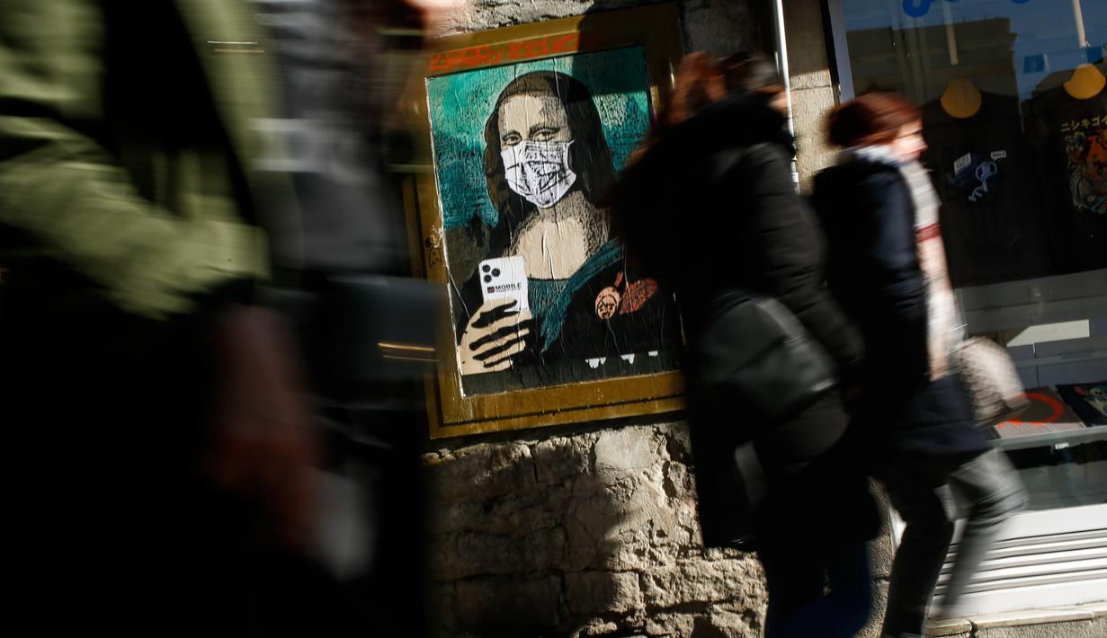 Orang-orang berjalan melewati poster seniman Italia Salvatore Benintende yang menggambarkan Mona Lisa karya Leonardo da Vinci mengenakan masker dan memegang smartphone yang bertuliskan "Mobile World Virus" di sebuah jalan di kota Barcelona, Spanyol pada Selasa (18/2/2020). (PAU BARRENA/AFP)