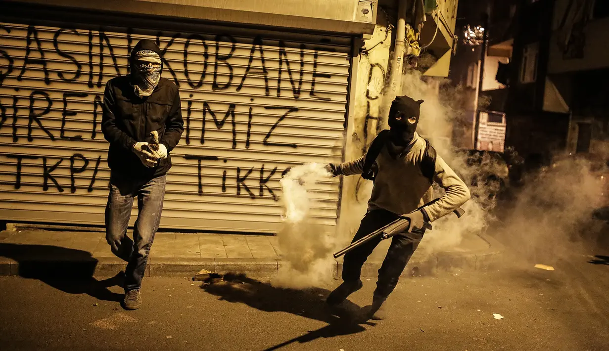 Dua militan Kurdi bersiap melemparkan tabung gas air mata ke arah polisi anti huru hara Turki dalam bentrokan di distrik Okmeydani, Istanbul (15/12/2015). Bentrokan terjadi karena pemerintah memberlakukan pembatasan jam malam. (AFP Photo/ Cagdas Erdogan)