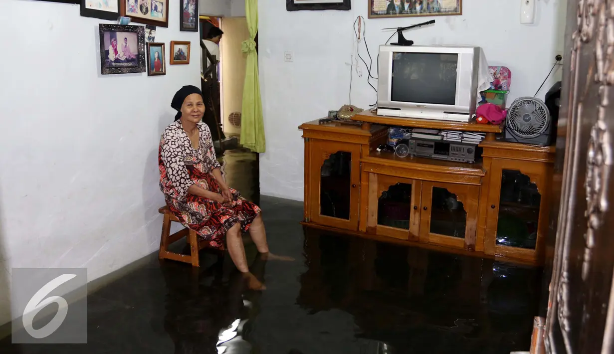 Warga duduk di dalam rumahnya yang tergenang air akibat banjir di kawasan Jatayu, Jakarta, Senin (21/11). Banjir disebabkan tingginya curah hujan dan buruknya saluran air serta meluapnya Kali Pesanggrahan. (Liputan6.com/Gempur M. Surya)