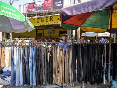 Seorang pedagang menata celana panjang sambil menunggu pelanggan pakaiannya di salah satu ruas jalan, Surabaya, Jawa Timur, pada Minggu 19 April 2026. Badan Pusat Statistik (BPS) Republik Indonesia akan melaksanakan Sensus Ekonomi 2026 (SE2026). (JUNI KRISWANTO/AFP)
