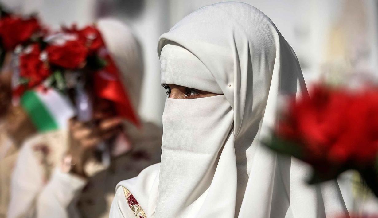 Sejumlah mempelai perempuan terlihat duduk berdampingan dengan riasan dan gaun putih. Tampak dalam foto, seorang calon pengantin wanita memperhatikan acara perayaan pernikahan massal untuk pasangan Palestina yang diselenggarakan oleh Yayasan Bantuan Kemanusiaan Turki (IHH) di Kota Gaza pada 11 Mei 2026. (Omar AL-QATTAA/AFP)