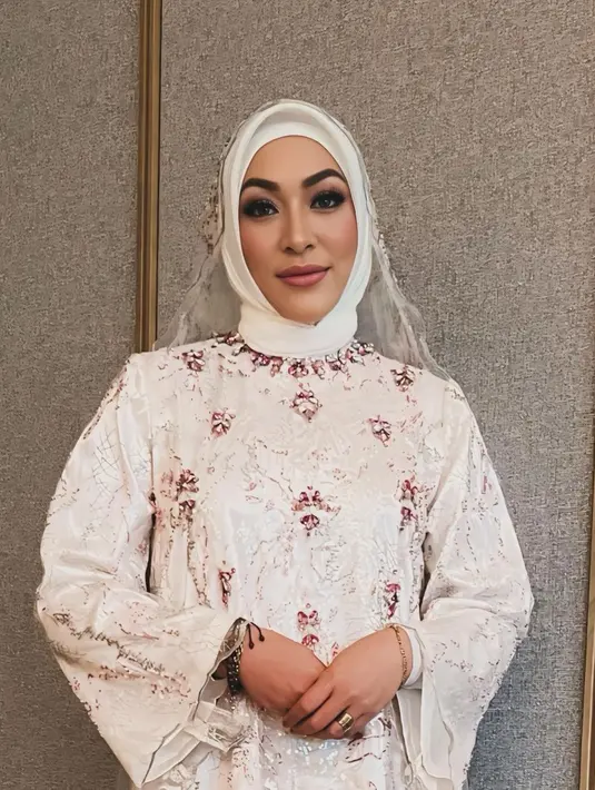 Penampilan Angelina Sondakh di momen pengajian tak kalah memesona. Ia tampil dalam balutan dress brokat putih dengan aksen beads warna pink. Penampilanya dilengkapi dengan hijab segi empat putih dan kerudung senada. [@rezaartameviaofficial/@angelinasondakh09].