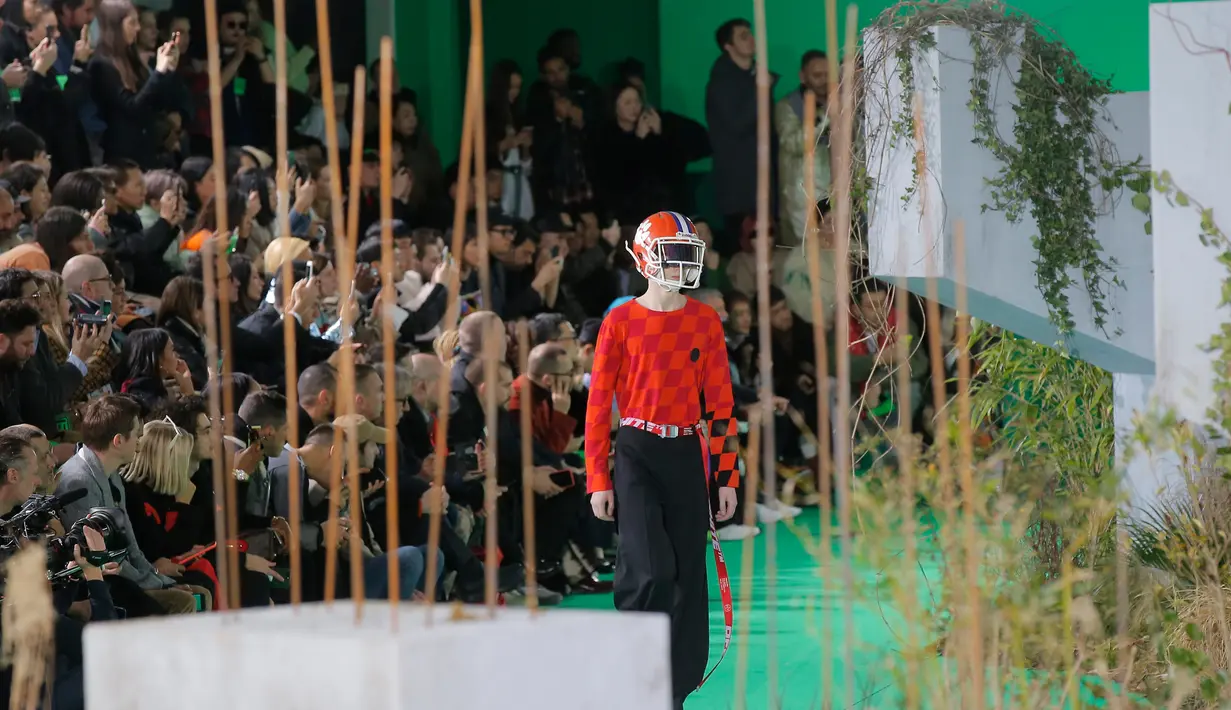 Seorang model membawakan rancangan koleksi Fall/Winter 2019 dari brand Off-White pada Paris Fashion Week, Rabu (16/1). Dalam perhelatan itu, sejumlah model mengenakan helm futbol, saat melenggang di catwalk. (AP/Michel Euler)
