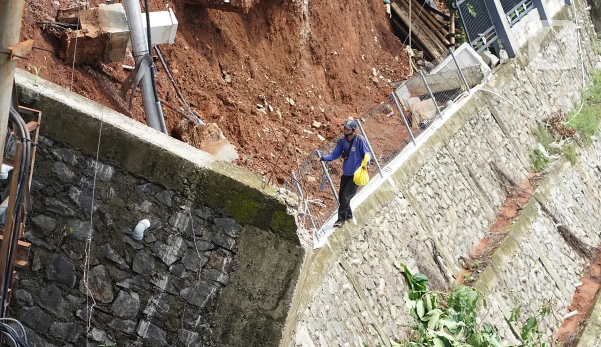 Petugas melintas di dekat turap yang hancur di Jalan Damai, Ciganjur, Jakarta Selatan, Minggu (11/10/2020). Hujan yang deras sejak Sabtu (10/10/2020) sore mengakibatkan kawasan tersebut mengalami banjir sekaligus longsor. (Liputan6.com/Immanuel Antonius)