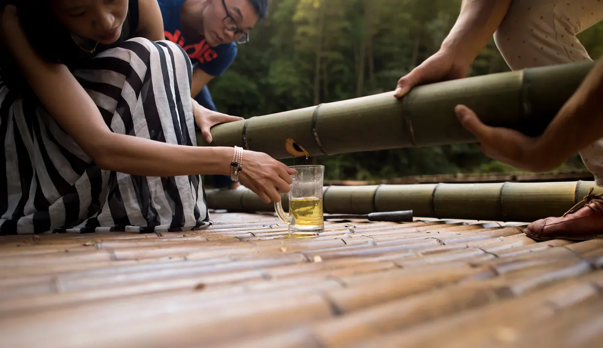 Pengunjung bersiap menikmati langsung minuman beralkohol yang telah disimpan di dalam batang bambu selama beberapa bulan di Hutan Yibin, China pada 30 Juli 2016. (AFP Photo/Fred Dufour)